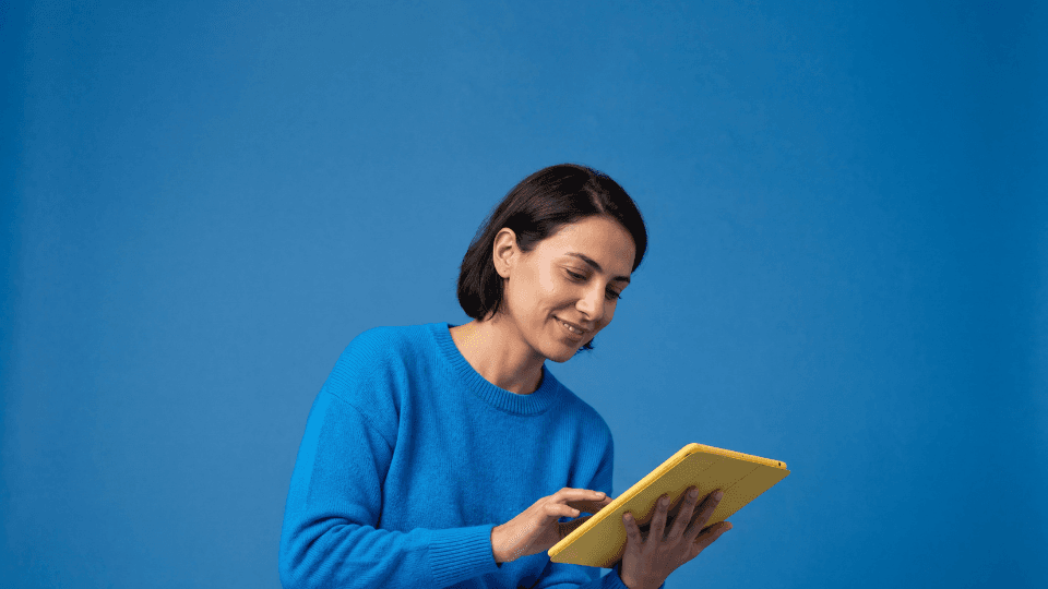 woman in blue cardigan looking at yellow tablet