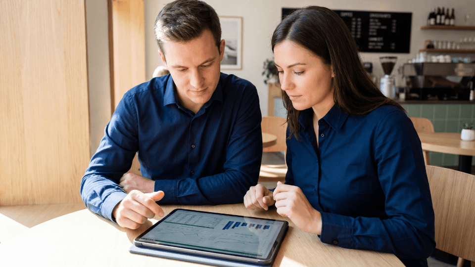 Woman and man in blue shirts looking at data in tablet